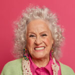 studio shot of happy delighted elderly woman smiles positively, being well dressed, feels energized in old age, expresses positive emotions, isolated on pink bright background. mature people